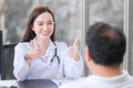 Asian beautiful woman doctor smiles and shows thump up sign or Ã¢â¬ÅVery goodÃ¢â¬Â with her patient due to his healthcare at hospital